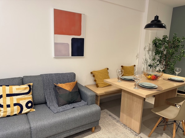 Un salon moderne avec un canapé gris, une table à manger en bois et un tableau abstrait aux lignes épurées.