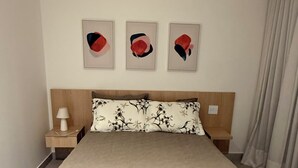 Une chambre d’hôtel avec un lit, une table de chevet, une lampe et trois œuvres d’art encadrées accrochées au mur.
