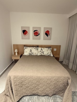 Une chambre d’hôtel avec un lit, une table de chevet, une lampe et trois œuvres d’art encadrées accrochées au mur.
