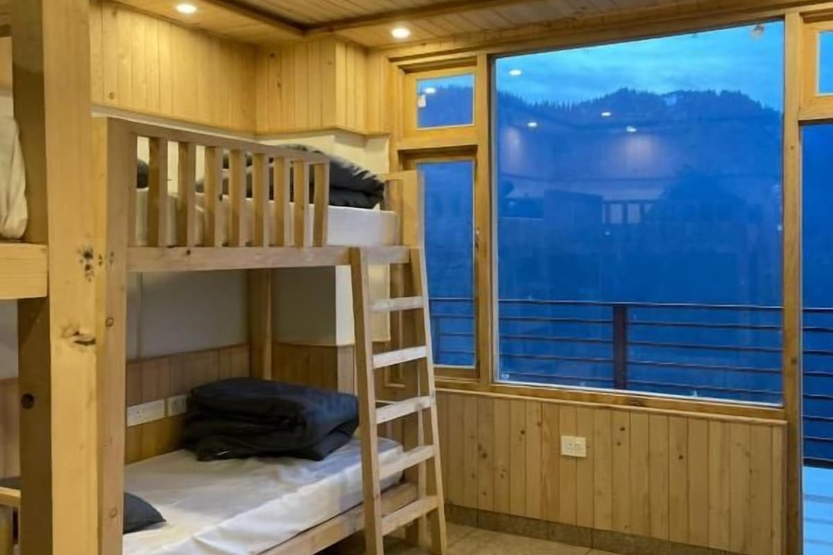 Une chambre avec des lits superposés, une échelle et une grande fenêtre donnant sur un plan d’eau et des collines.