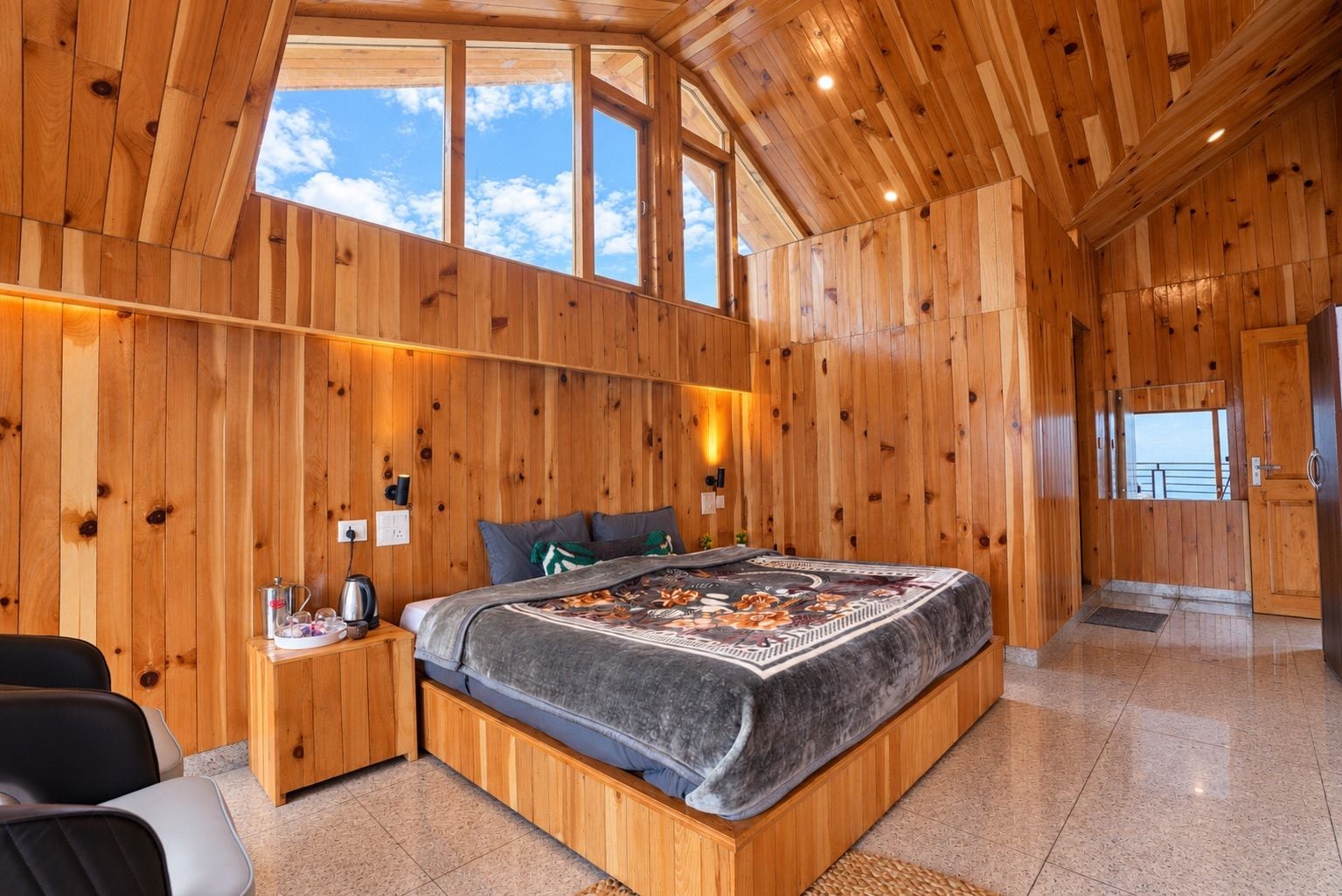 Dormitorio con paneles de madera, una cama grande, mesitas de noche y vistas por las ventanas.