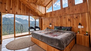 Ein Schlafzimmer mit einem großen Bett, Holzwänden und einem Balkon mit Blick auf die Berge.