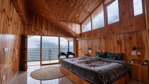 Ein Schlafzimmer mit Holzvertäfelung, einem großen Bett, zwei Stühlen, Blick ins Freie und einem Balkon.
