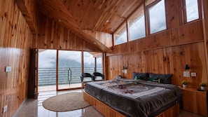 Une chambre à coucher au décor intérieur en bois, avec un grand lit, deux fauteuils, une vue sur l’extérieur et un balcon.