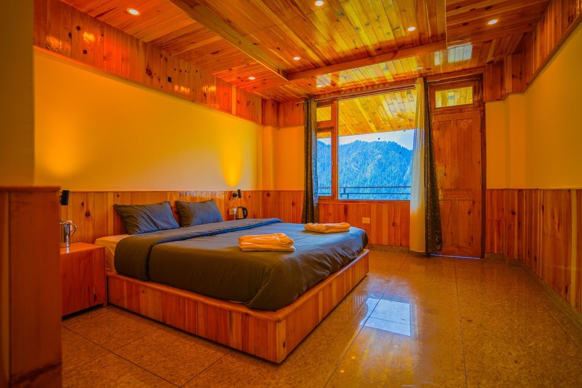 Un intérieur en bois comprenant un lit, une table de chevet et une fenêtre donnant sur la montagne.