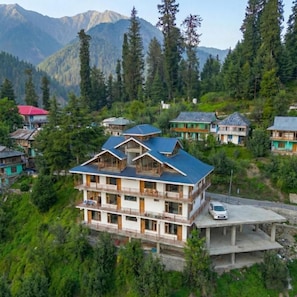 Un immeuble à plusieurs étages doté de balcons, entouré d’une forêt dense et de montagnes.