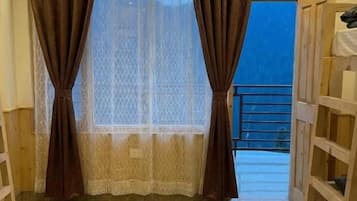 A room with a wooden floor, a window with brown curtains, and a view of a balcony.