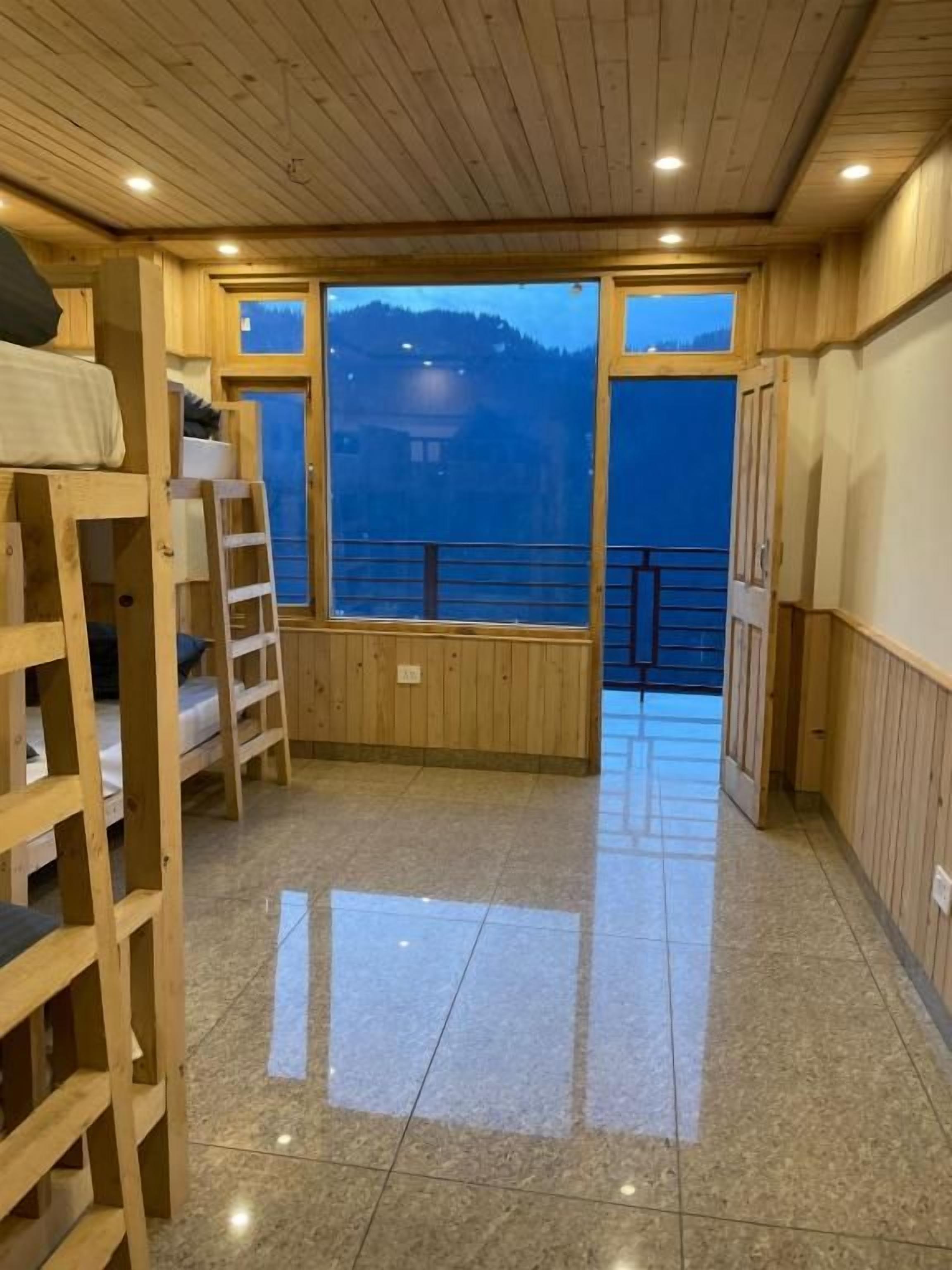 Una habitación con literas, una escalera, un ventanal con vistas a montañas y un balcón.