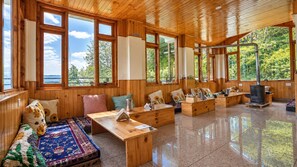 A wooden cabin interior with large windows, a fireplace, and a cozy seating area. - Nesto Stay and Cafe (Shoja)