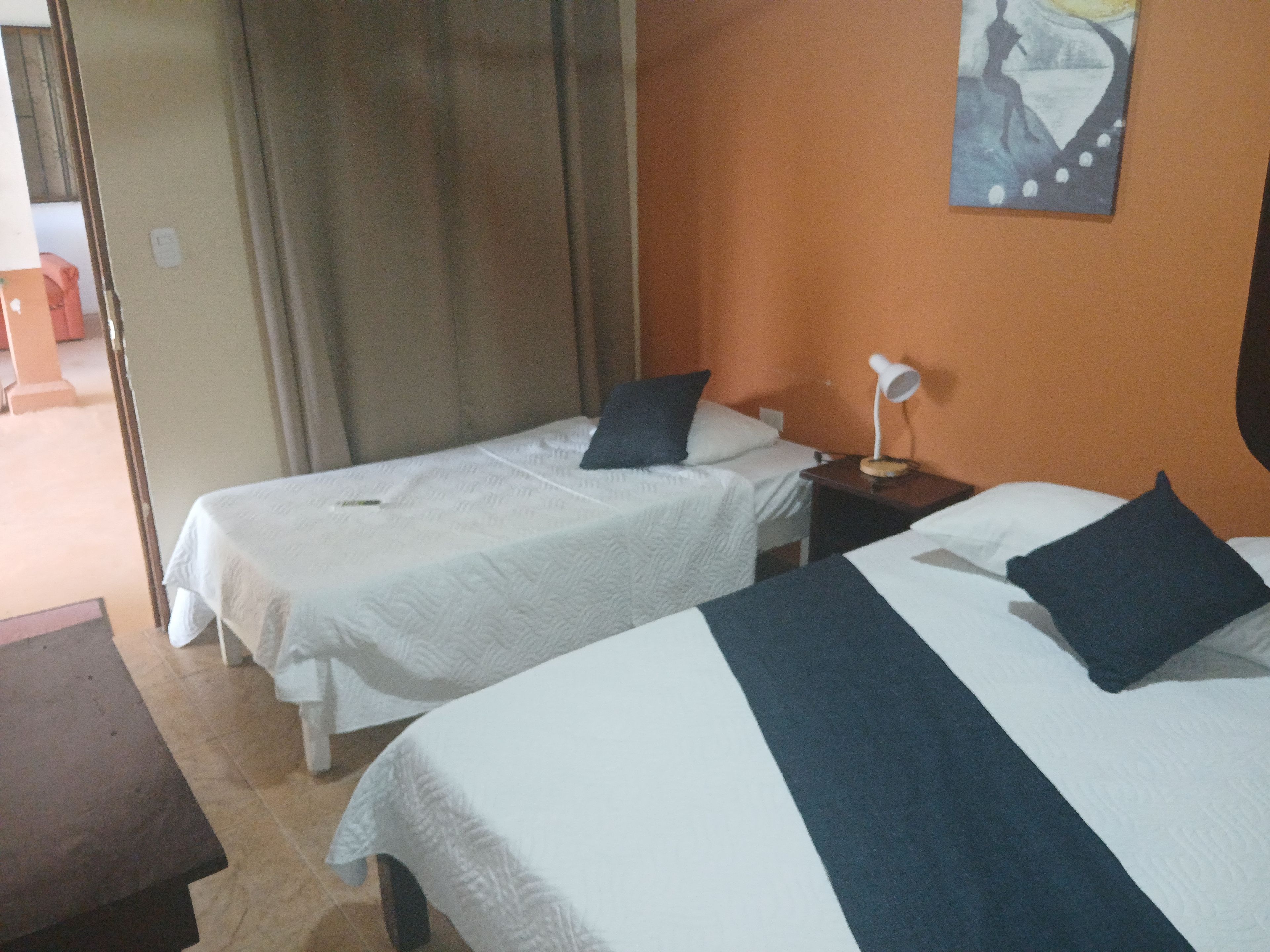 A hotel room with two single beds, a nightstand with a lamp, and a painting on the wall.