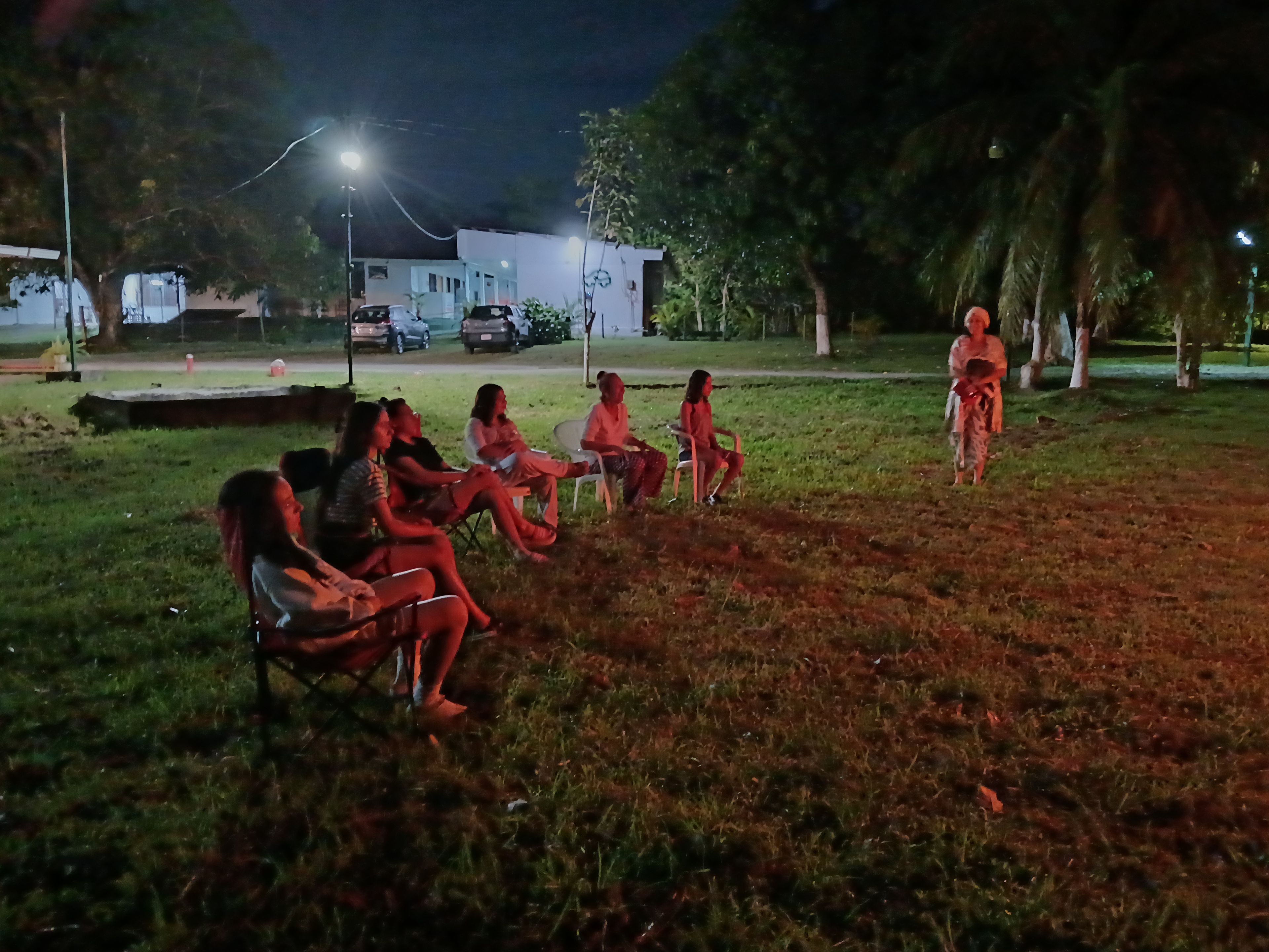 A group of people seated on lawn chairs in an outdoor setting at night.