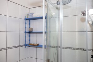 A bathroom with white tiled walls, a glass shower enclosure, and blue shelves with toiletries. - An oasis of peace in the heart of Valle Gran Rey (Valle Gra Rey)