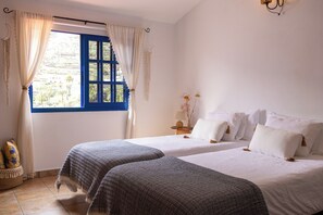 A bedroom with two beds, a window with blue shutters, and a view of palm trees outside. - An oasis of peace in the heart of Valle Gran Rey (Valle Gra Rey)