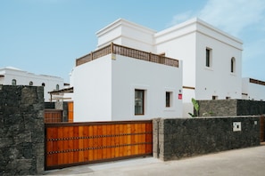 A modern white building with a stone wall and a wooden gate. - Villa in Lanzarote | Pool | Volcanic Garden (Yaiza)