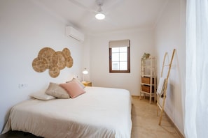 A bedroom with a bed, a wall-mounted air conditioner, a window with a view, a wooden ladder, and a shelf with baskets. - Villa in Lanzarote | Pool | Volcanic Garden (Yaiza)