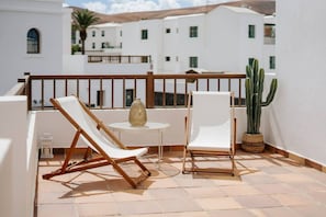 A balcony with two white lounge chairs, a small round table with a vase, and a potted cactus. - Villa in Lanzarote | Pool | Volcanic Garden (Yaiza)