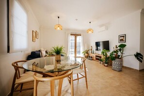 A modern living room with a glass dining table, wooden chairs, a sofa, and a TV. - Villa in Lanzarote | Pool | Private Garden (Yaiza)