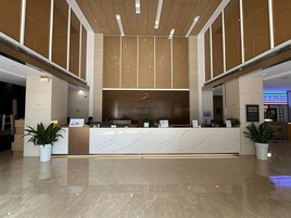 Una moderna reception con piano in marmo, affiancata da piante in vaso, in un'ampia hall con soffitto alto e pavimento lucido.