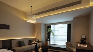 Una habitación de hotel moderna con cama, sofá, escritorio, silla, planta en maceta y un amplio ventanal.