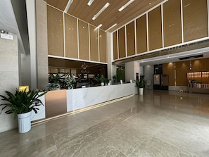 Vestíbulo moderno de hotel con mostrador de recepción de mármol, plantas en macetas y una araña.