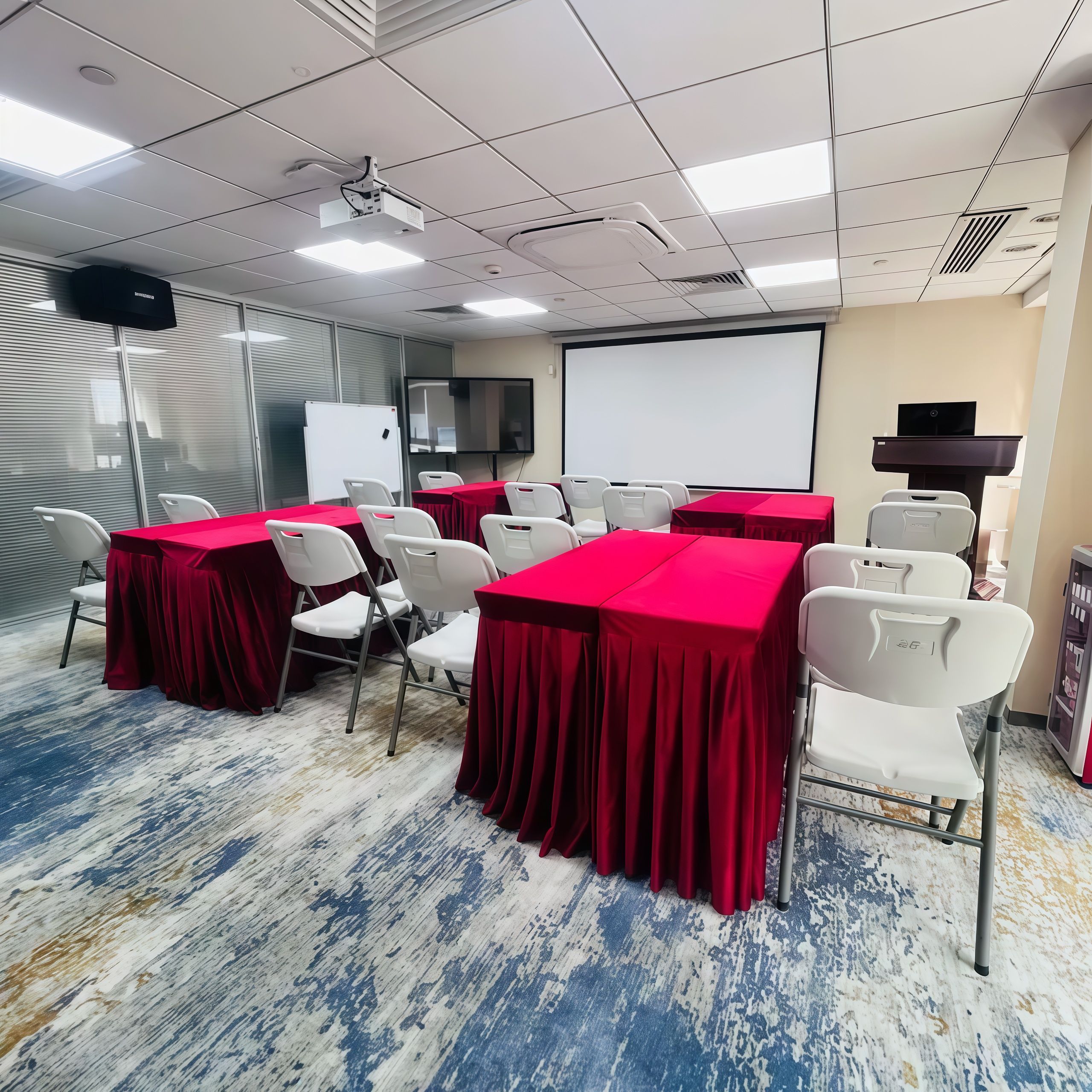 Una sala conferenze con tavoli, sedie, un proiettore, uno schermo e una lavagna.