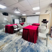 A conference room with tables, chairs, a projector, a screen, and a whiteboard.