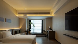 Habitación de hotel con cama, escritorio, silla, televisor y una planta.