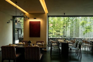 A modern dining area with a large window, a red abstract painting, and bamboo outside.