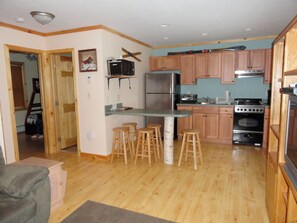 A compact kitchen with wooden cabinets, a refrigerator, a stove, and bar stools.