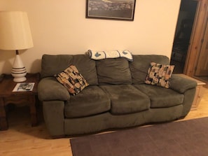A green sofa with patterned cushions, a white lamp, and a framed picture on the wall. - "Inn The Pines" 2-bedroom apartment in charming Jay, NY (Jay)
