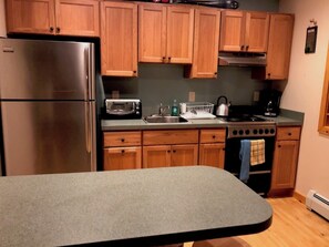 A kitchen with wooden cabinets, a stainless steel refrigerator, a toaster, a kettle, and a stove. - "Inn The Pines" 2-bedroom apartment in charming Jay, NY (Jay)