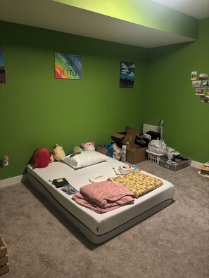 Ein Schlafzimmer mit einem Bett, Kissen, Kuscheltieren, einer Bilderwand und einer grünen Wand.