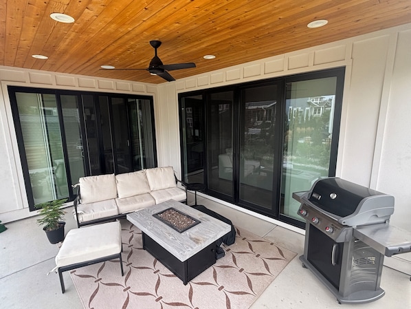 Eine Terrasse im Freien mit einer Couch, einem Feuerkorb, einem Grill und großen Schiebeglasfenstern.