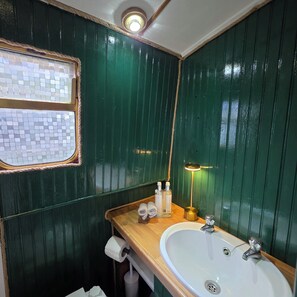 Et badeværelse med et trækommode, en hvid vask, et spejl og et lille vindue med mosaikdesign.