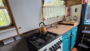 Una kitchenette funcional con estufa, lavamanos y ventana con cortinas de encaje.