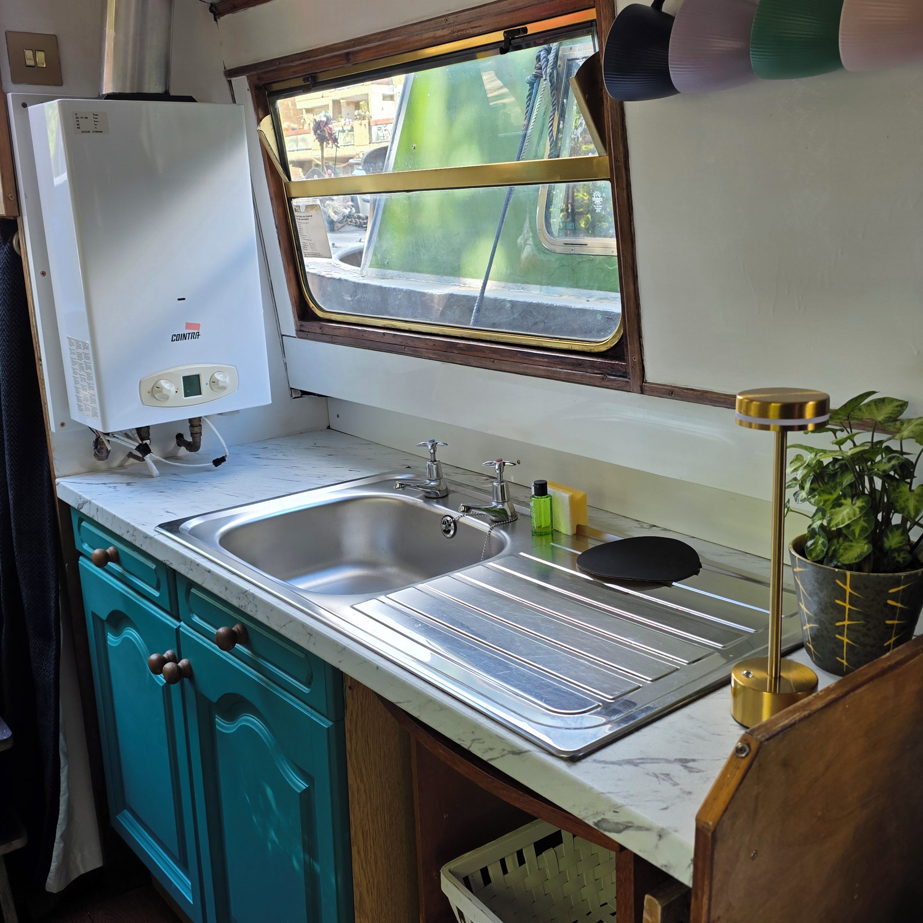 A compact kitchen with a built-in water heater, a sink, and a window overlooking a street.