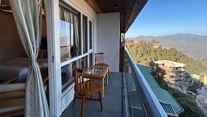 A balcony with a view of a mountainous landscape, a sofa, and two wooden chairs. - Hotel Dwaper by Aventra Retreat  (Mussoorie)