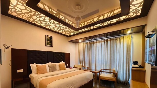 A hotel room with a large bed, a desk, a chair, a ceiling fan, and a window with curtains. - Hotel Dwaper by Aventra Retreat  (Mussoorie)