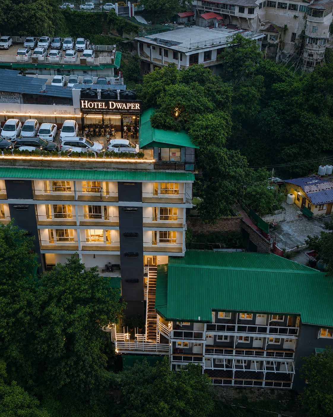 Un hotel de varios pisos con techo verde, múltiples balcones y un estacionamiento.