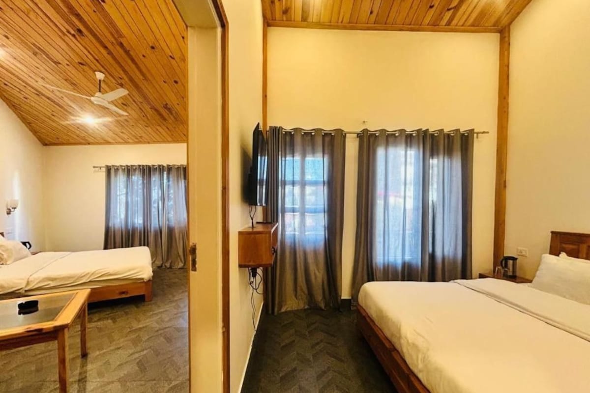 Ein Hotelzimmer mit zwei Betten, Holzboden, Fernseher und Vorhängen.