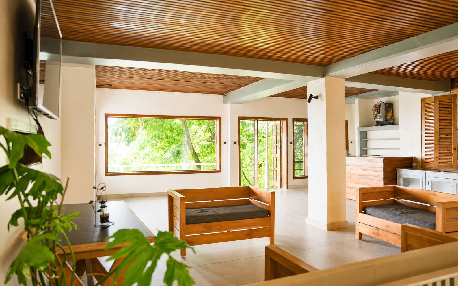 A spacious living area with a wooden ceiling, large windows, and a kitchenette.