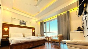 A hotel room with a large bed, a desk, a chair, and a sofa. There is a window with curtains and a view of the sky. - Hotel Dwaper by Aventra Retreat  (Mussoorie)