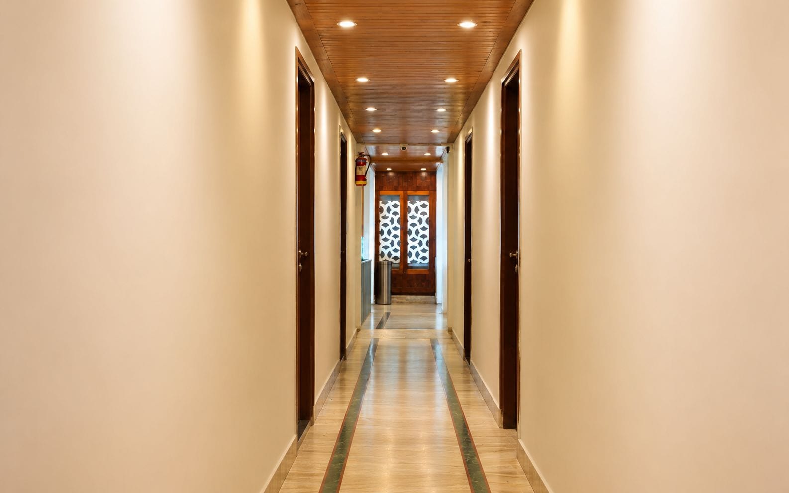 Un pasillo de hotel con techo de madera, paredes color beige y piso estampado.