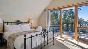 Un dormitorio con cama, mesita de noche, lámpara y vistas al exterior a través de un ventanal.