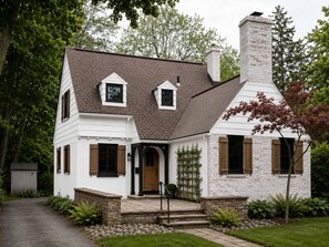 A two-story house with a brick chimney, white exterior walls, and a front porch with steps leading to the entrance. - Charming Renovated Cape Cod Near Strong Hospital & U of R (Rochester)