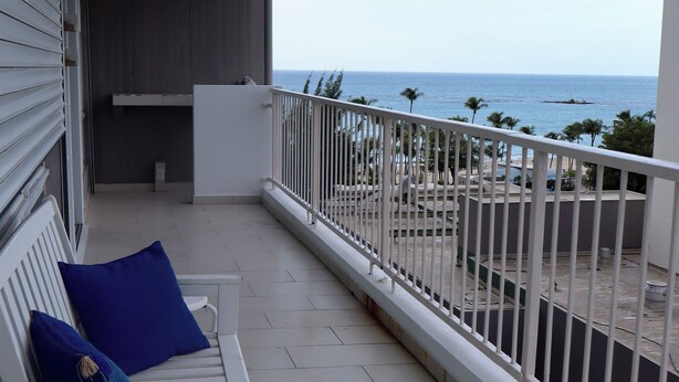 Un balcón con mobiliario blanco, una pequeña mesa y vistas a la playa y al océano.
