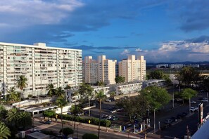 Un edificio residencial de varios pisos con balcones, una zona de estacionamiento y palmeras.