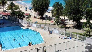 Una piscina con gente, una playa y un cielo azul despejado.