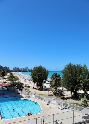 Una piscina con gente, una playa y un cielo azul despejado.