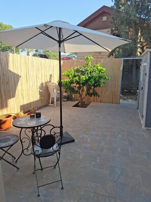 Un patio con una mesa y sillas, un paraguas grande, plantas en macetas y una cerca de madera.